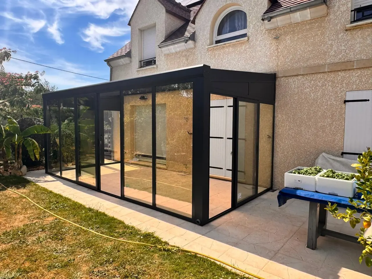 Véranda anthracite et baies vitrées au pied d’une maison.