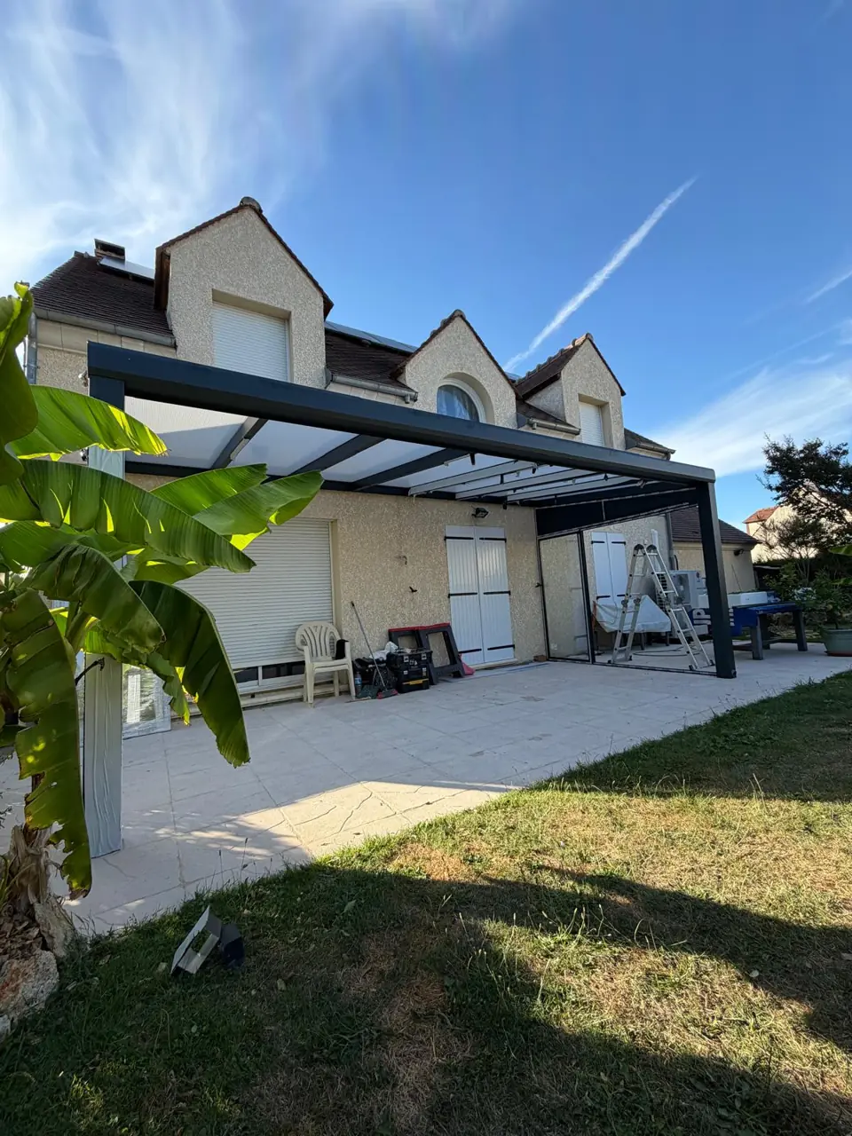 Pergola anthracite et terrasse aménagée au pied d’une maison.